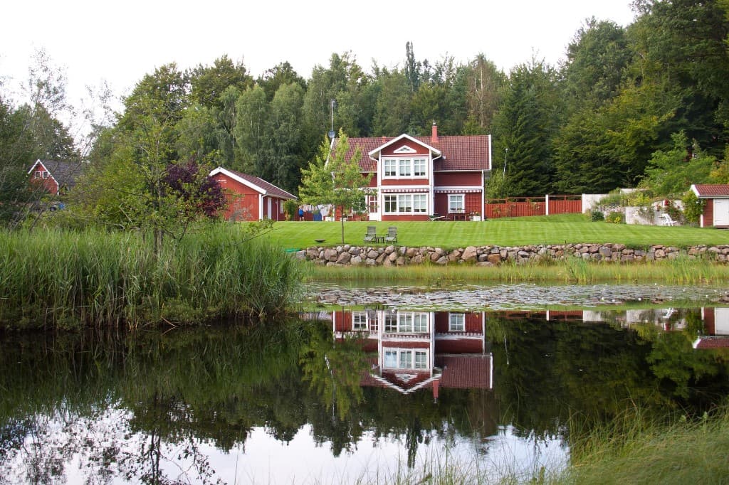 Röd svensk villa speglad i vatten — privat bostadsförsäljning