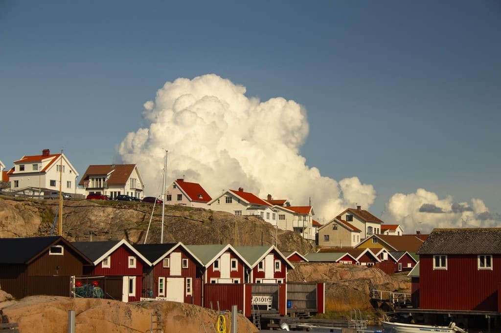 Röda sjöbodar och hus längs västkustklippor under sommarhimmel