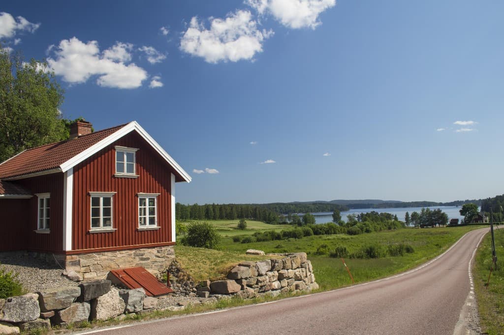 Röd stuga vid sjö och landsväg